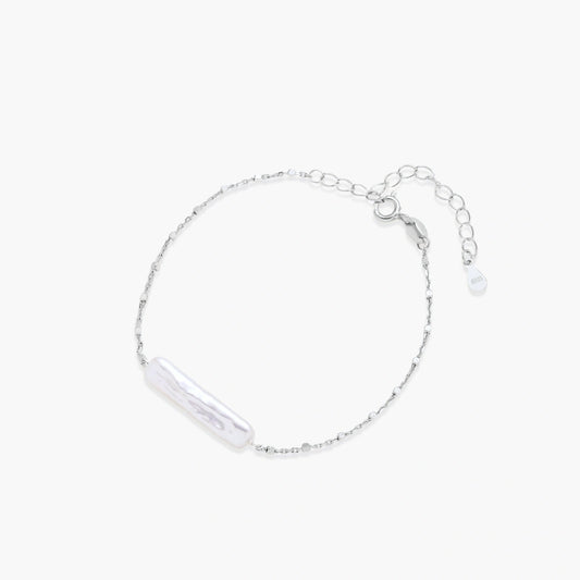 Minimalist bracelet featuring a long, rippled baroque pearl on a delicate chain with an adjustable extender.