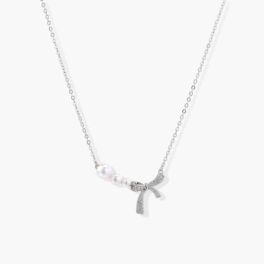 Delicate silver-tone necklace featuring a central pavé bow and three graduated freshwater pearls.