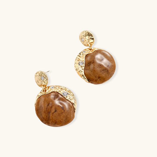 Gold-toned dangle earrings with organic brown resin stones and crystal accents on white background