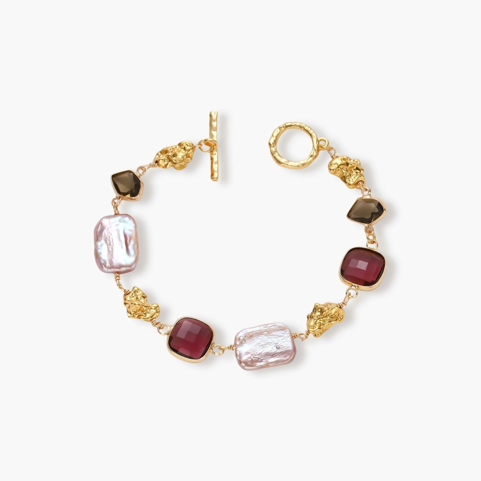 18k gold-plated copper bracelet with burgundy stones, smoky quartz, baroque pearls and ornate golden charms on white background.