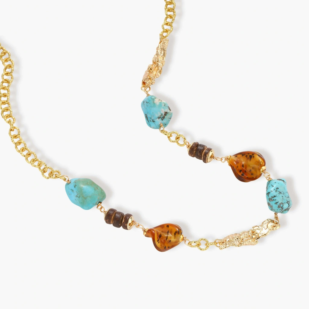 Statement necklace with gold chain, turquoise stones, amber beads, and wooden elements on cream background.