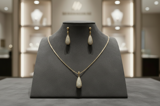 Gold-plated teardrop necklace and earrings covered in AAA cubic zirconia crystals on cream background.