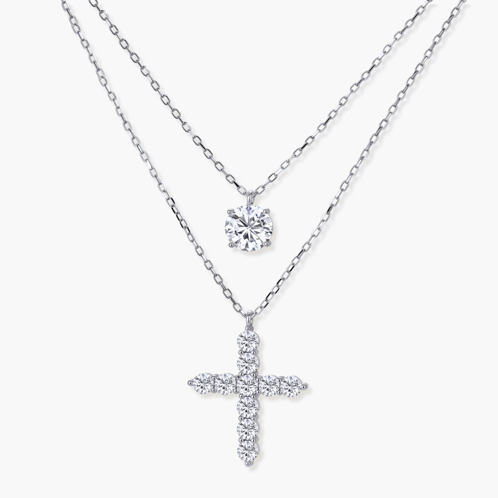 Layered sterling silver necklaces featuring a solitaire pendant and a cross pendant, elegantly displayed at varying lengths.