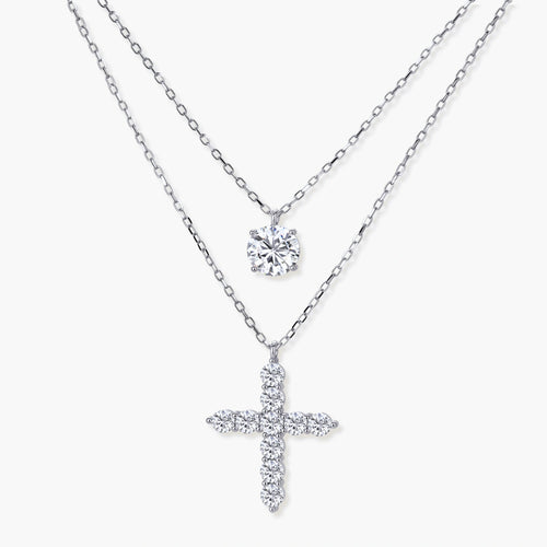 Layered sterling silver necklaces featuring a solitaire pendant and a cross pendant, elegantly displayed at varying lengths.