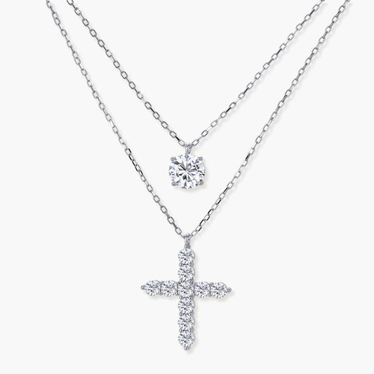 Layered sterling silver necklaces featuring a solitaire pendant and a cross pendant, elegantly displayed at varying lengths.