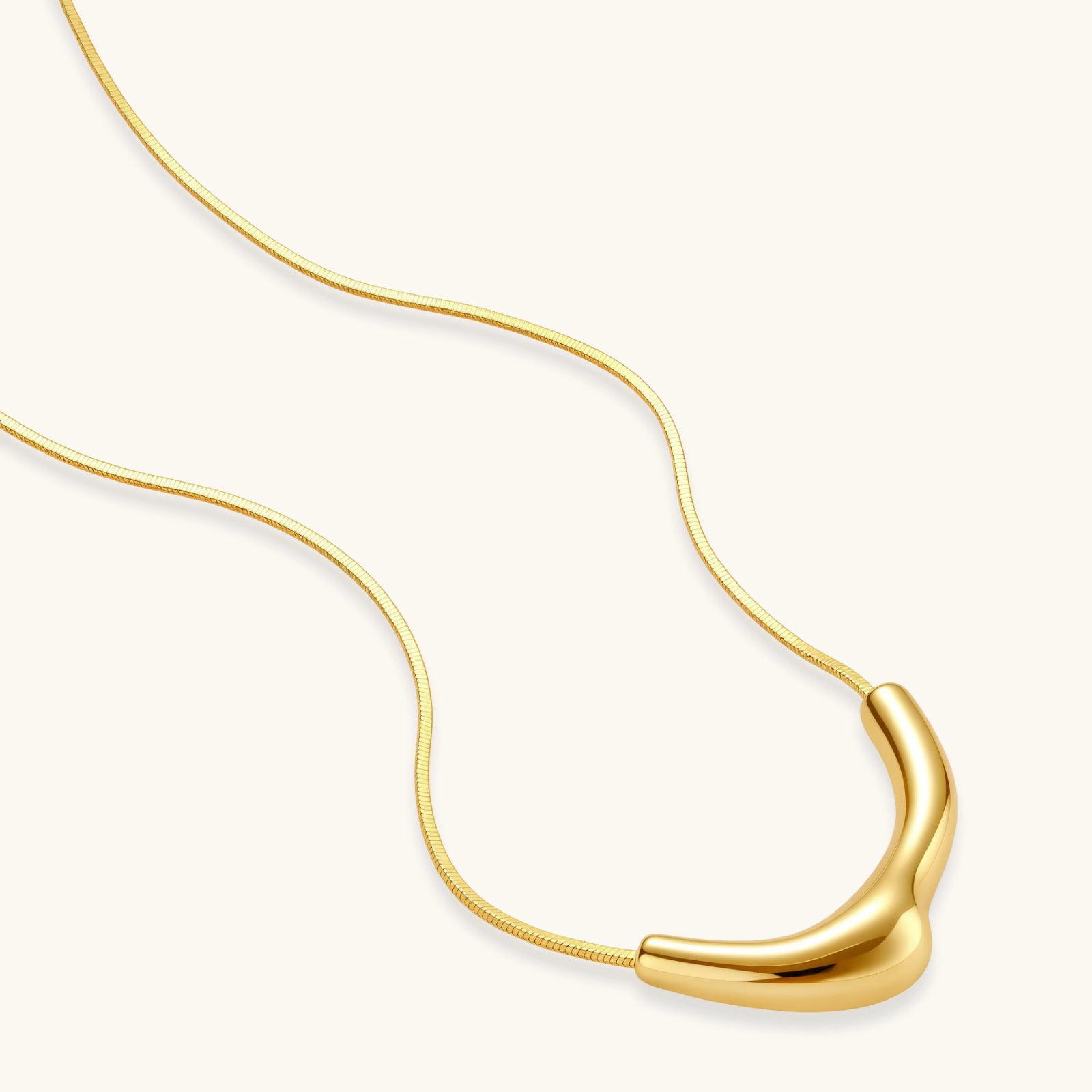 Minimalist gold-plated curved pendant necklace on delicate chain against cream background, showing adjustable length