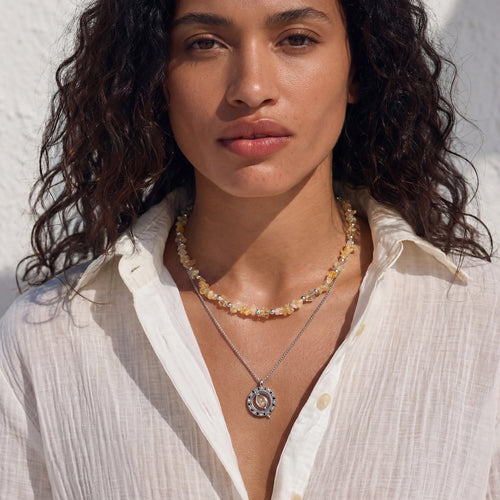 Layered necklace showcasing raw citrine-toned chips and a circular openwork pendant, elegantly worn with a light-coloured shirt.