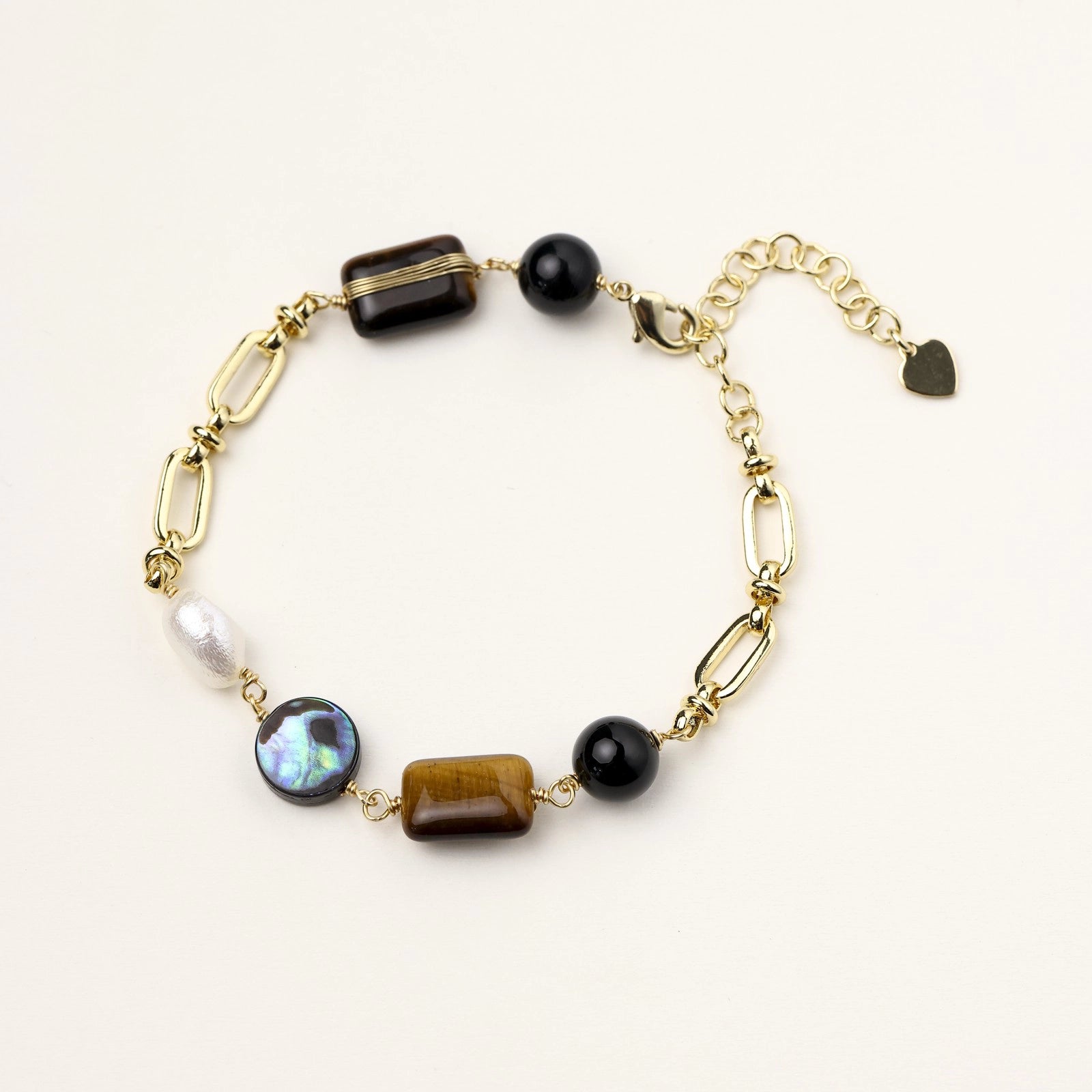 Gold paperclip chain bracelet featuring caramel tiger's eye, glossy black obsidian, iridescent pearl, and a heart charm.