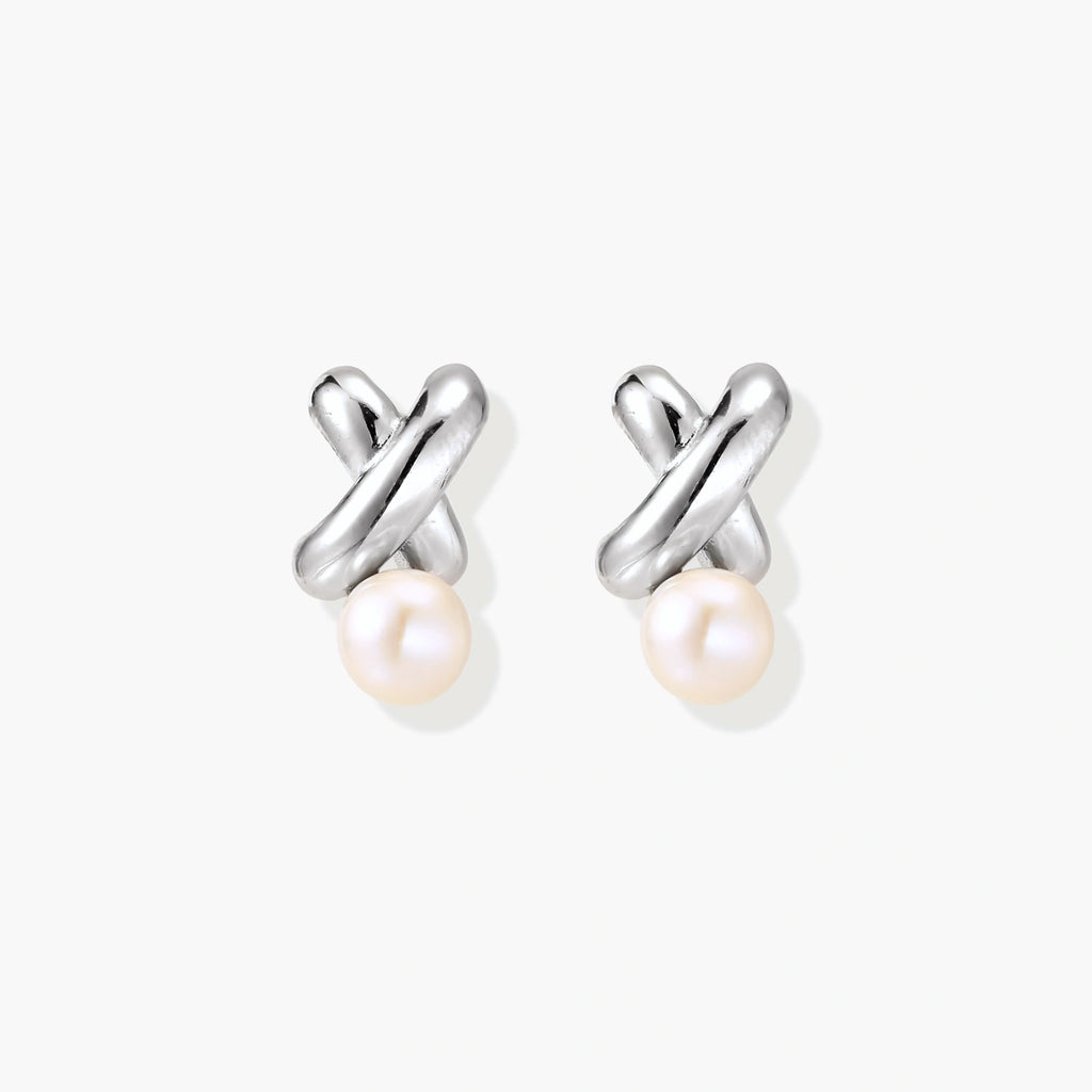 Rhodium-plated silver earrings with twisted X design and freshwater pearl drops on beige background
