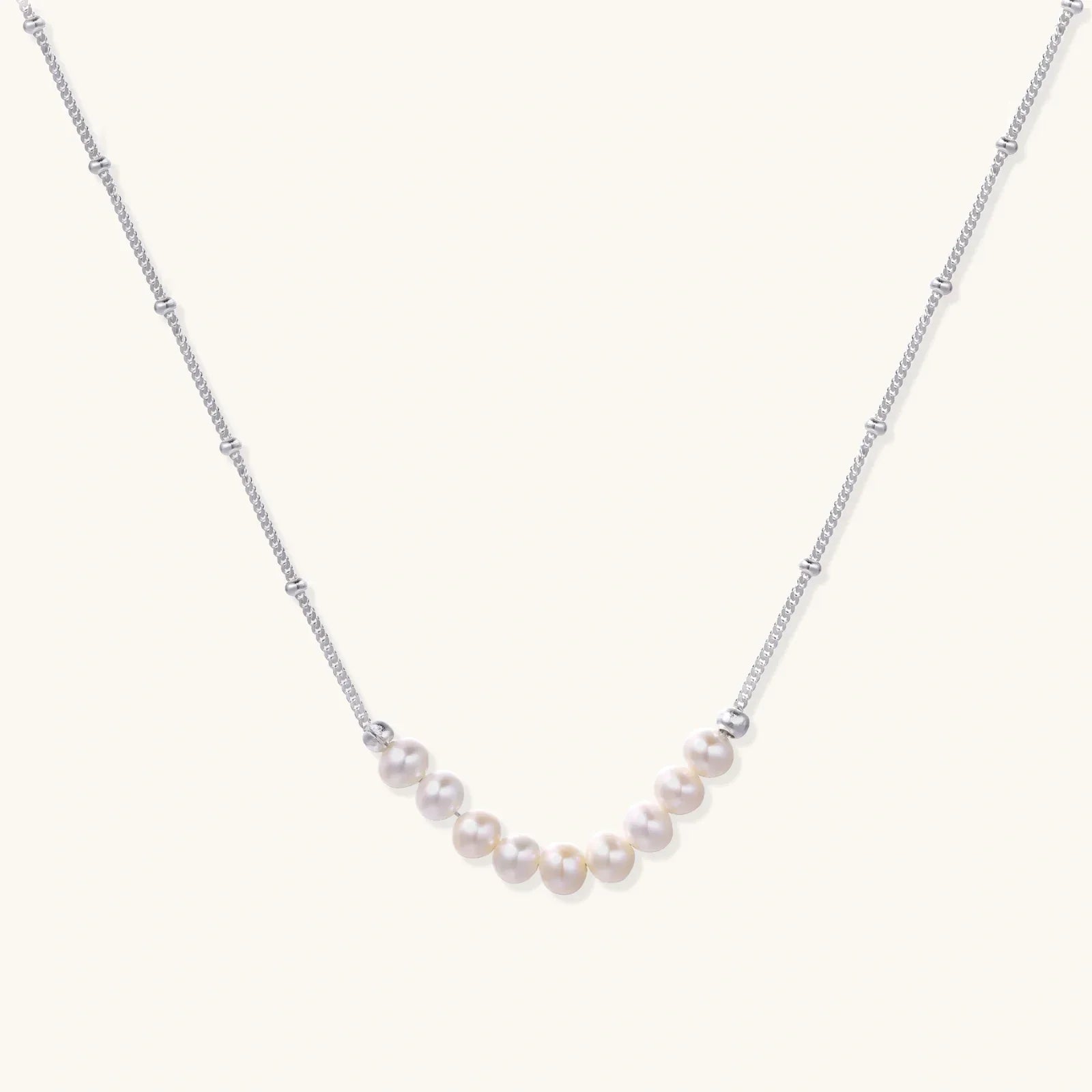 Delicate sterling silver chain necklace with small freshwater pearls arranged in a curved smile arc on cream background.