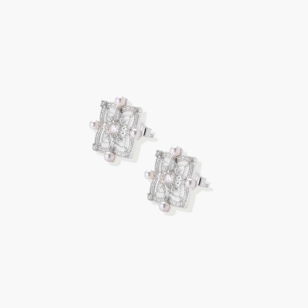Ornate sterling silver stud earrings with mandala-inspired filigree pattern and four freshwater pearls on beige background