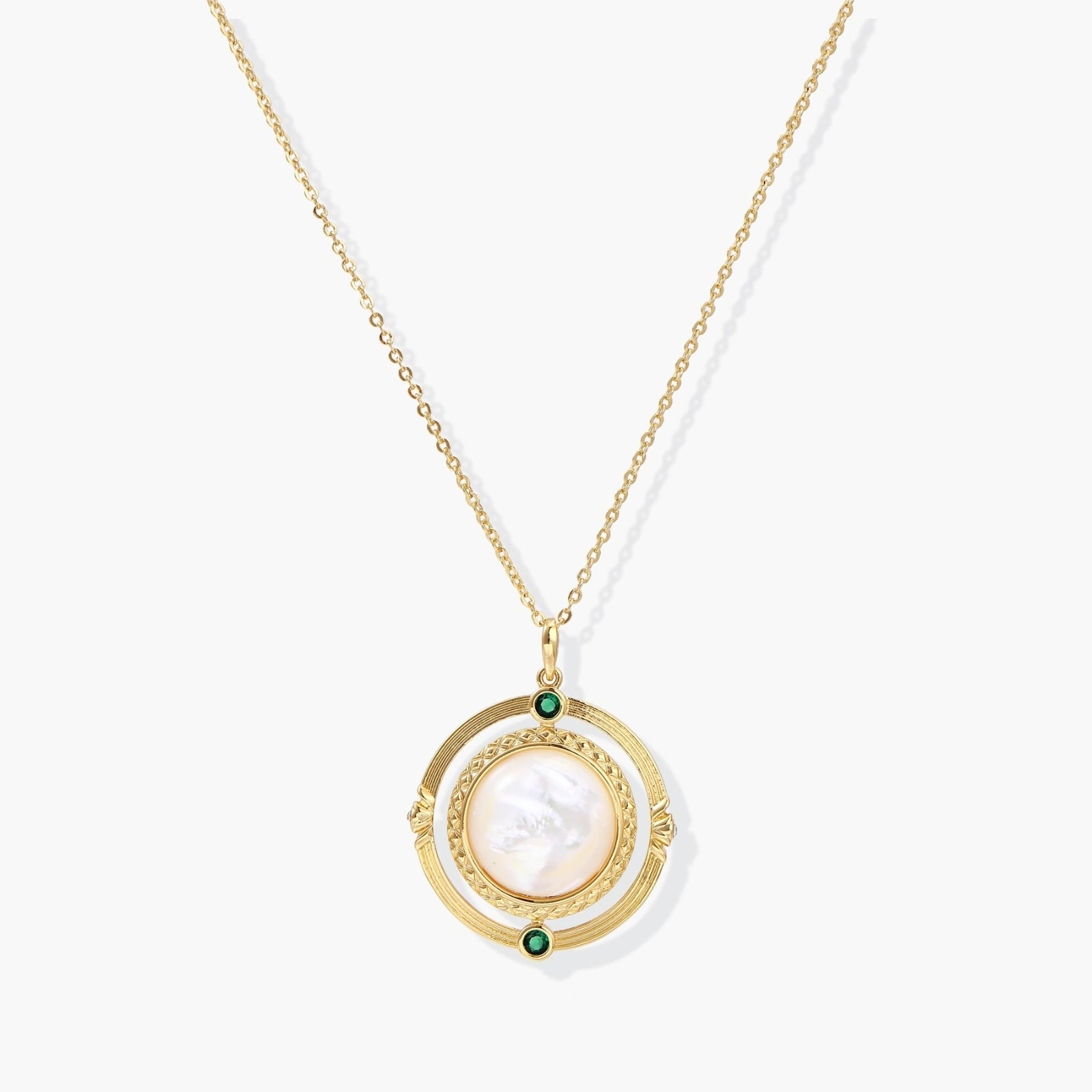 Gold pendant necklace featuring a circular design with a central mother-of-pearl disc and green zirconia accents.