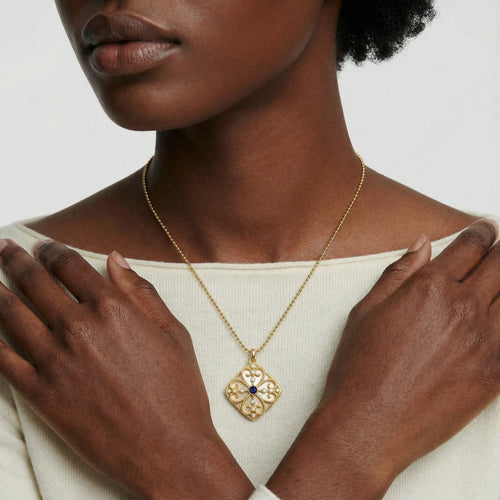 Ornate gold square pendant with intricate filigree and a deep blue lapis lazuli centre, suspended from a delicate ball chain.