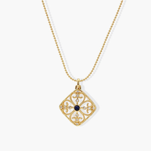 Ornate gold square pendant with intricate filigree and a deep blue lapis lazuli centre, suspended from a delicate ball chain.