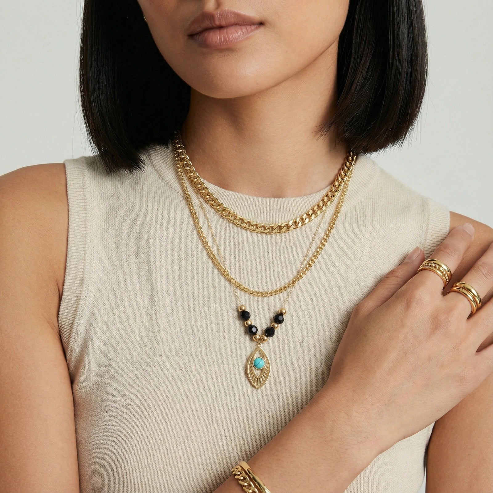 Layered gold necklace featuring a bold curb chain, delicate black quartz strand, and a striking turquoise eye pendant.