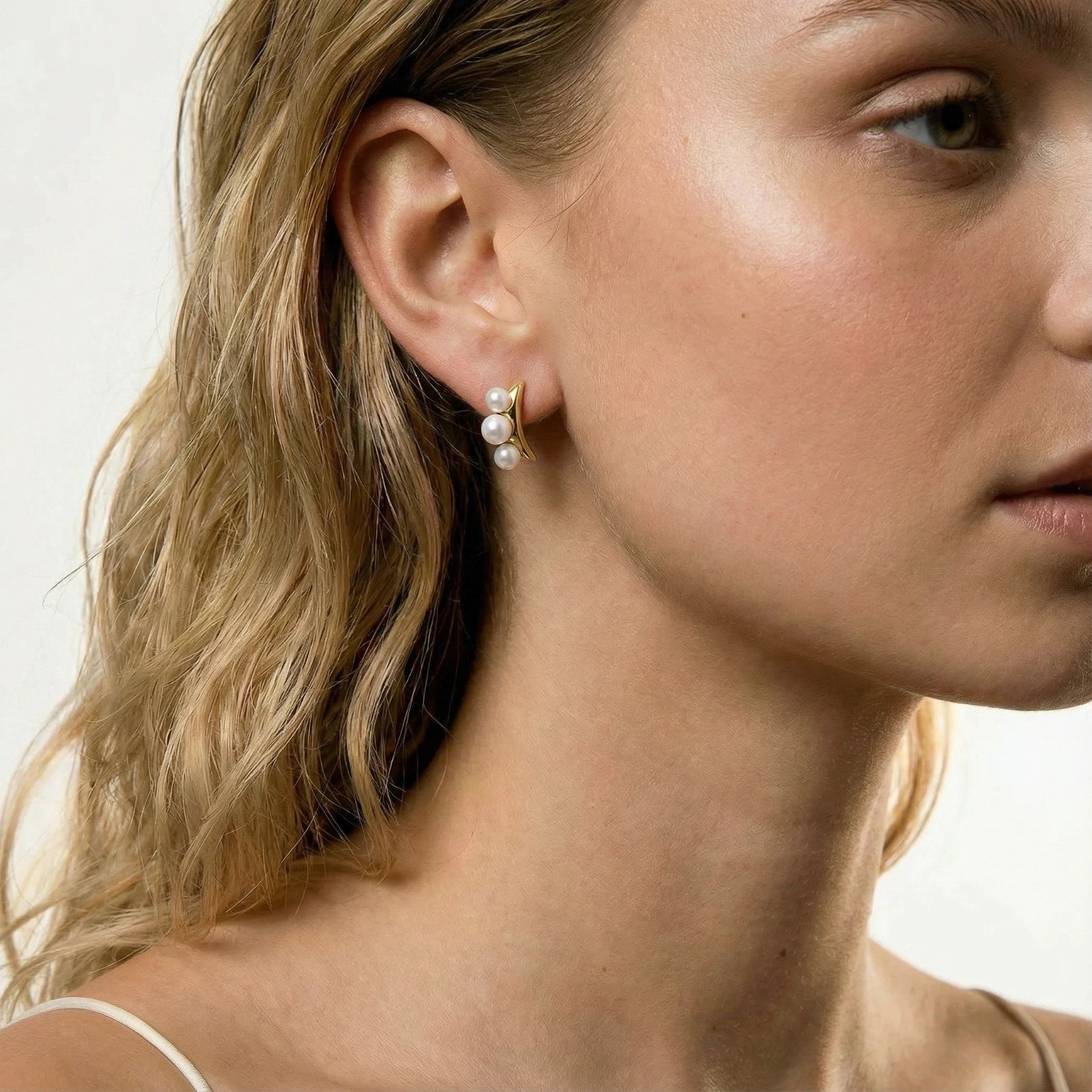 Close-up of a model wearing Pearl Trio Curve Studs, showcasing three freshwater pearls on a gracefully curved gold bar.