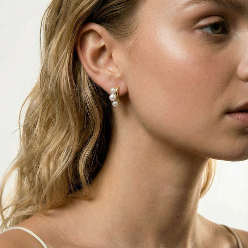 Close-up of a model wearing Pearl Trio Curve Studs, showcasing three freshwater pearls on a gracefully curved gold bar.