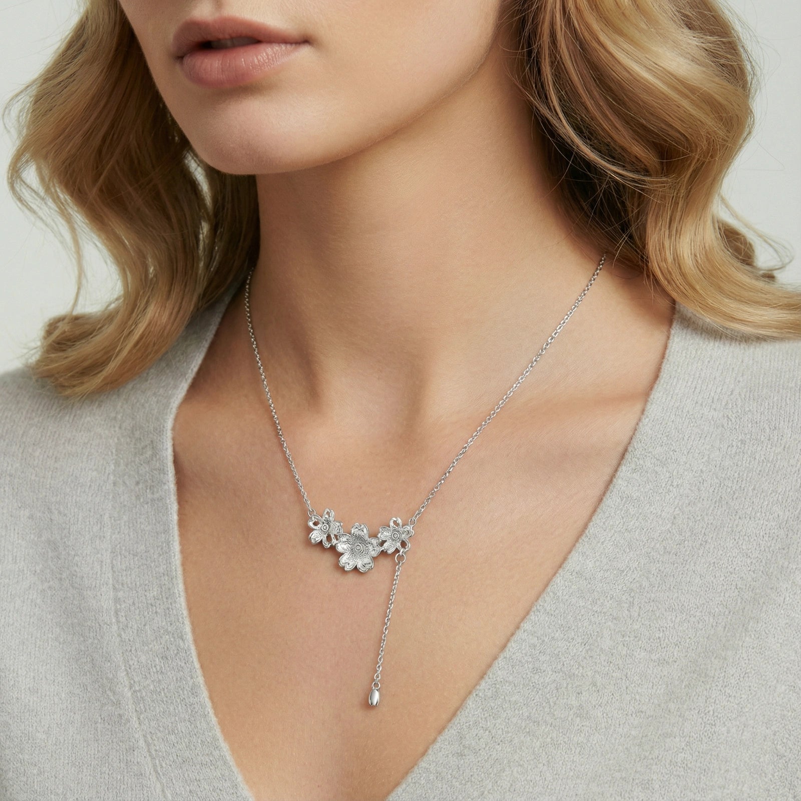 Lariat necklace featuring three silver-toned floral designs, elegantly worn around the neck with an adjustable chain.