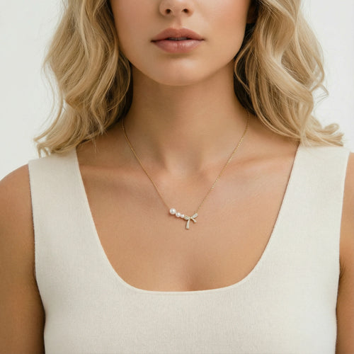 Delicate gold necklace featuring three small freshwater pearls and a stunning pavé bow, elegantly worn by a model.