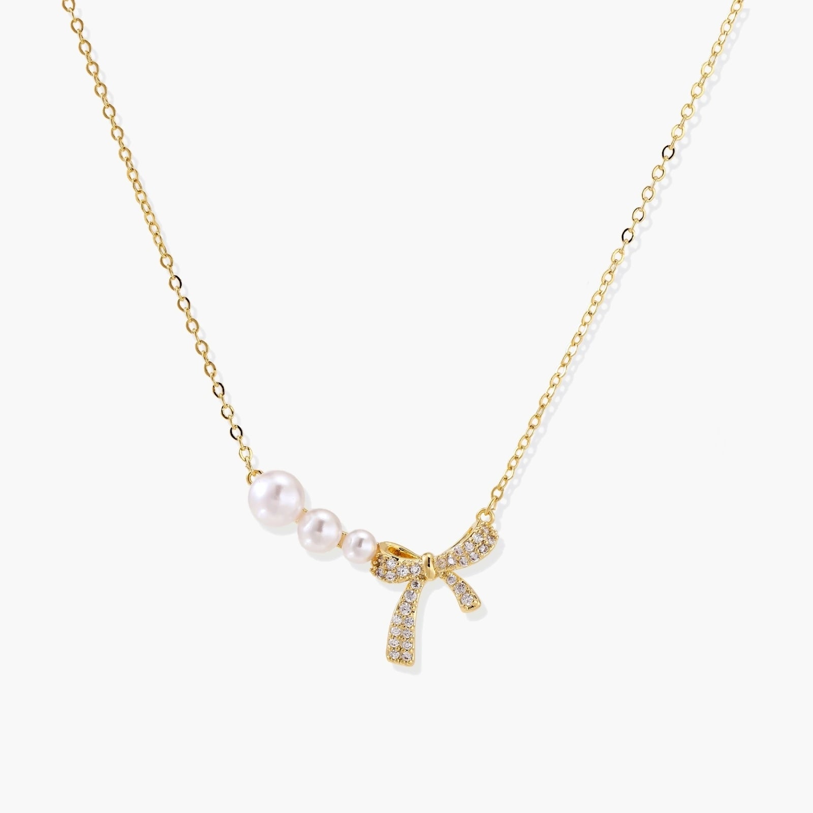 Delicate gold necklace featuring three small pearls and a crystal-embellished bow pendant.