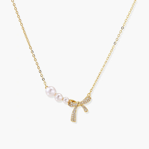 Delicate gold necklace featuring three small pearls and a crystal-embellished bow pendant.