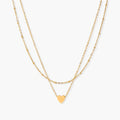 Delicate double-chain gold necklace with tiny heart pendant on cream background