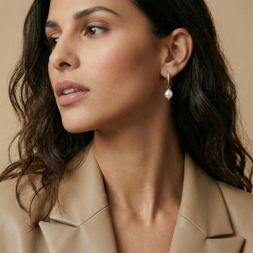 Gold huggie earrings featuring a dangling baroque pearl, elegantly showcased on a model's ear.