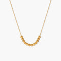 Delicate gold-plated necklace with graduated spherical beads forming gentle smile curve on beige background
