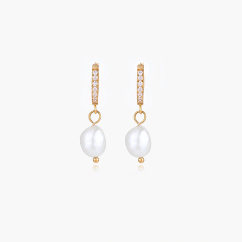 Gold huggie hoop earrings with pavé crystals and white freshwater pearl drops on cream background