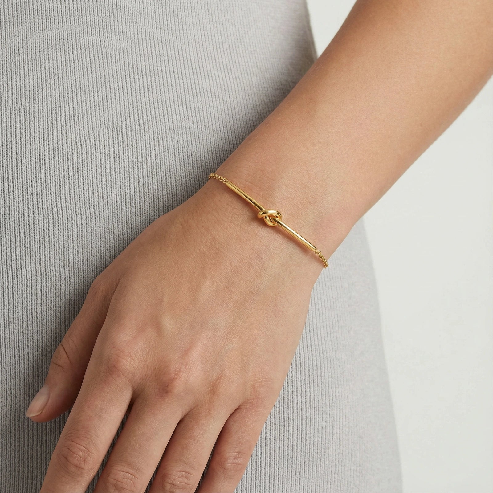 Delicate gold bracelet featuring a central twisted knot design, elegantly worn on the wrist.