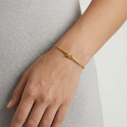 Delicate gold bracelet featuring a central twisted knot design, elegantly worn on the wrist.