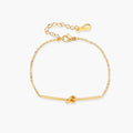 Delicate gold chain bracelet with minimalist bar and centered knot detail on cream background