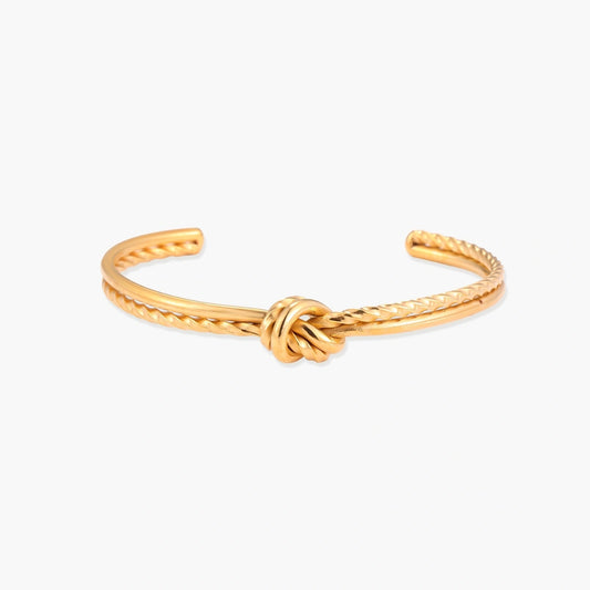 Gold cuff bracelet featuring a smooth and twisted band design with an elegant central knot.