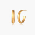 Chunky tubular hoop earrings in warm 14K gold-plated finish with smooth polished surface on cream background.
