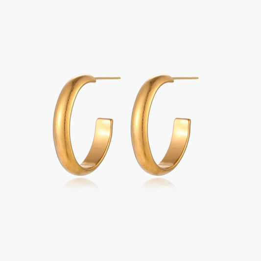 Chunky tubular hoop earrings in warm 14K gold-plated finish with smooth polished surface on cream background.