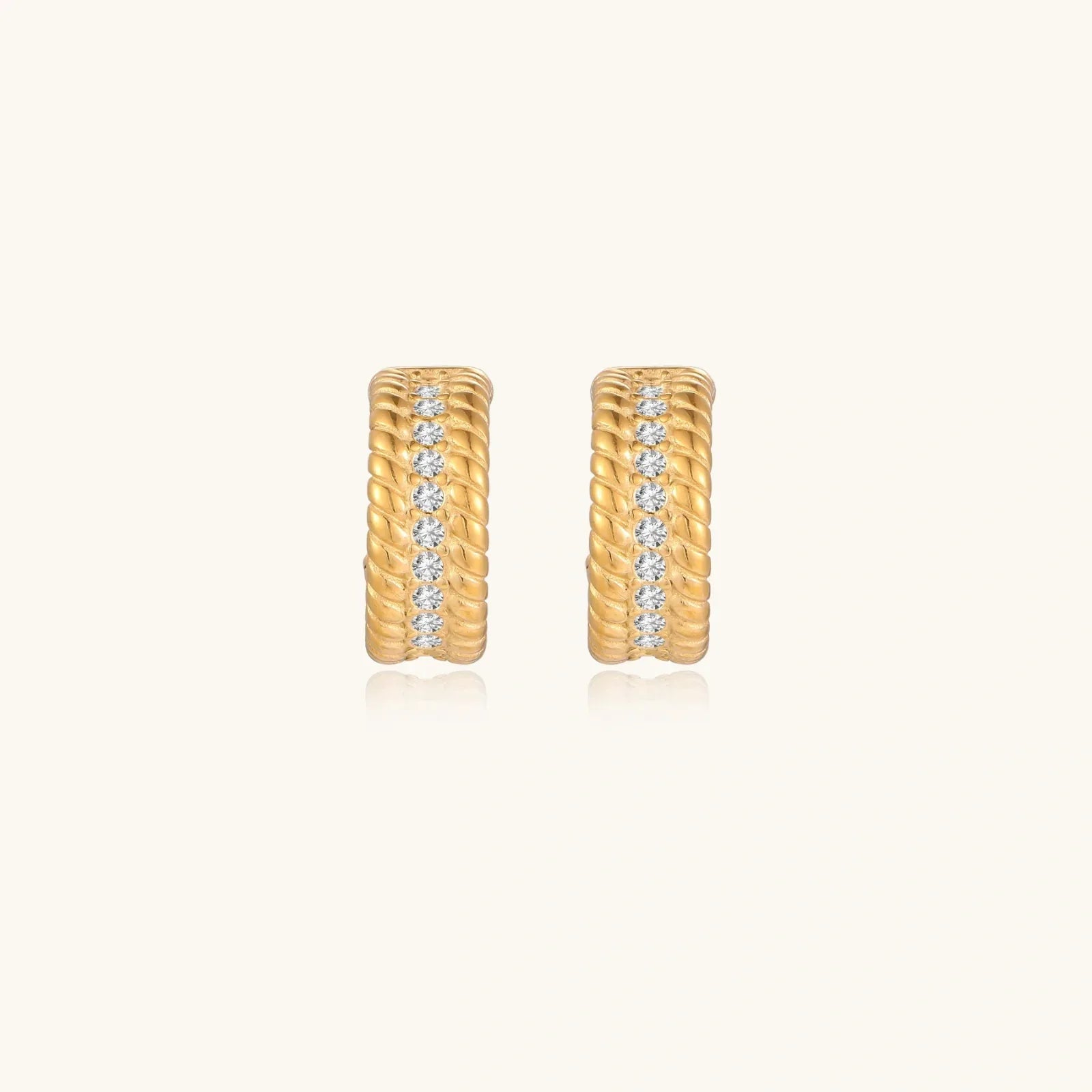 Textured gold huggie hoop earrings with raised ribbed rows creating dimensional sculptural design on cream background