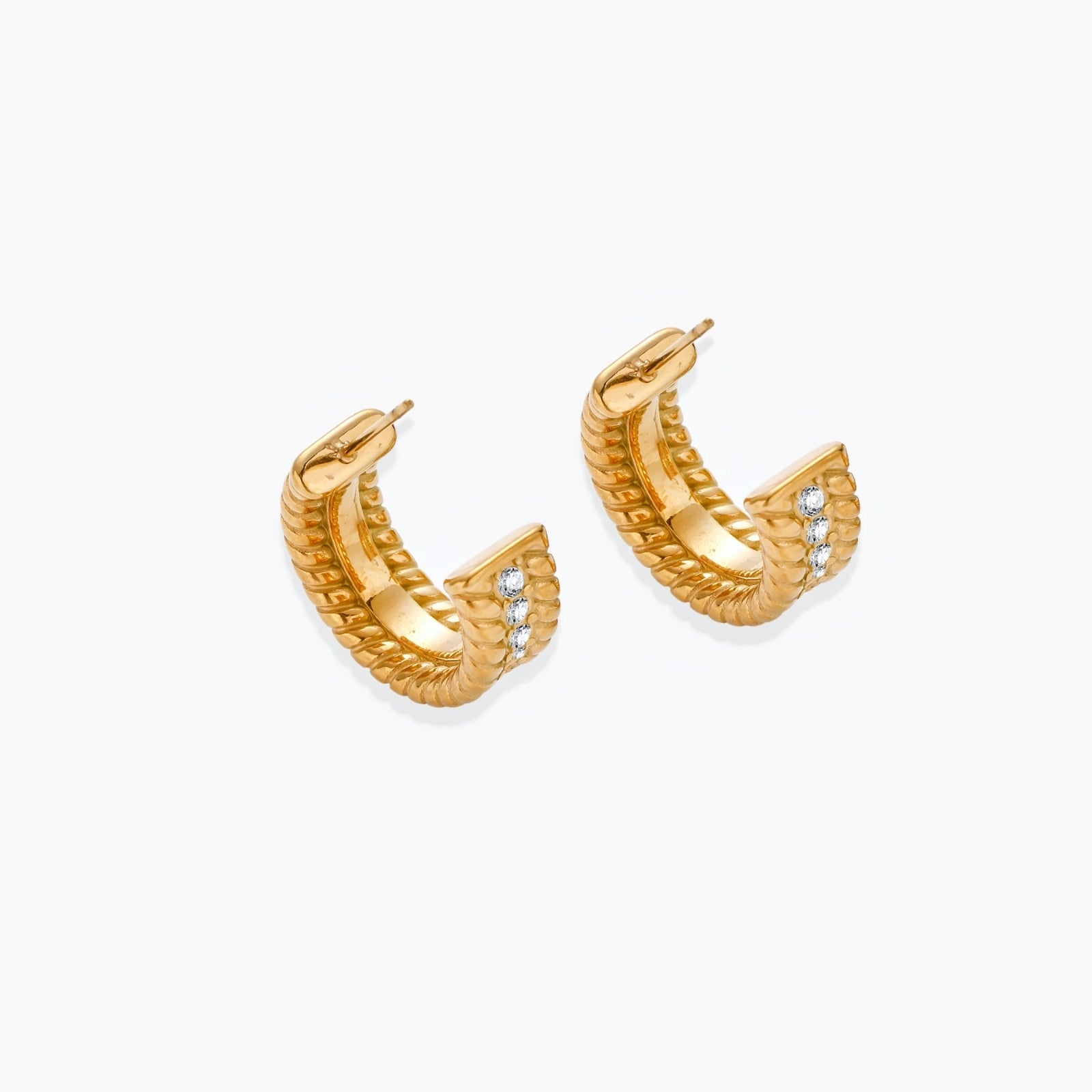 Textured gold huggie hoop earrings with raised ribbed rows creating dimensional sculptural design on cream background