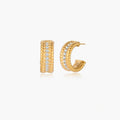 Textured gold huggie hoop earrings with raised ribbed rows creating dimensional sculptural design on cream background