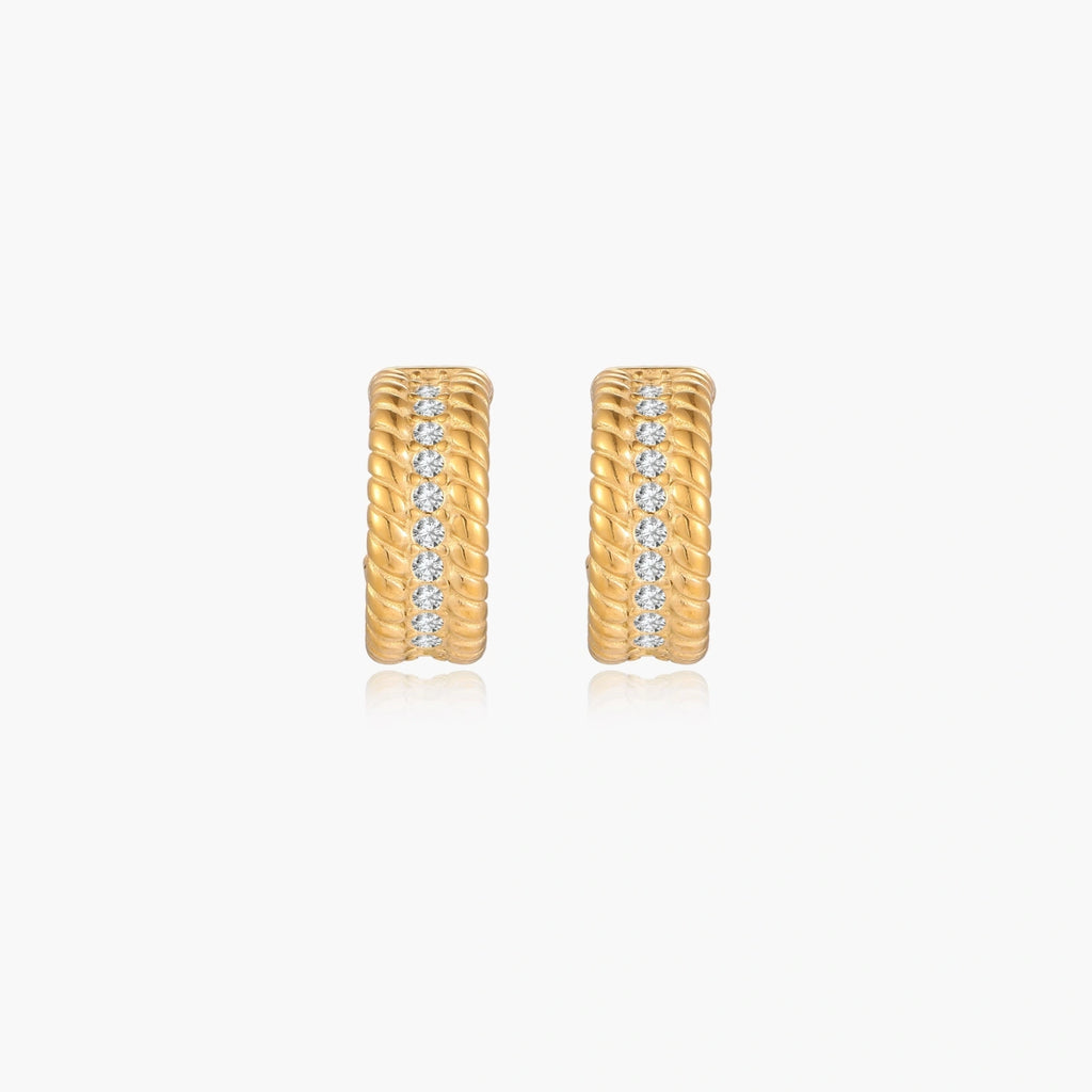 Textured gold huggie hoop earrings with raised ribbed rows creating dimensional sculptural design on cream background