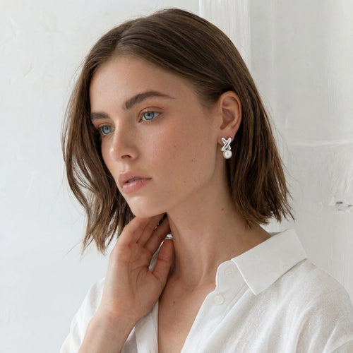 Model showcasing polished silver X design stud earrings with a round freshwater pearl, exuding elegance and sophistication.