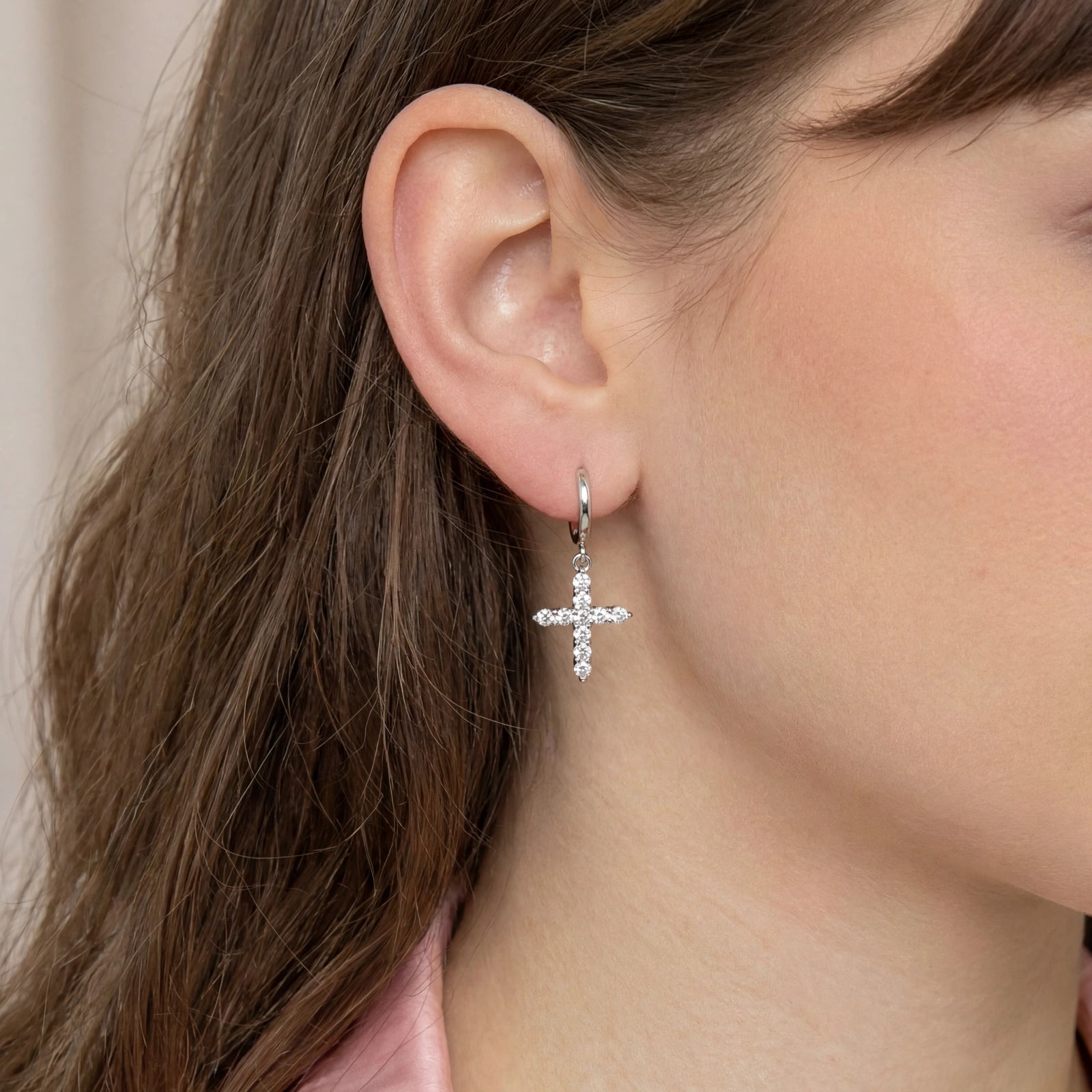 Hoop earrings featuring a swinging zirconia-set cross design, elegantly worn below the earlobe.