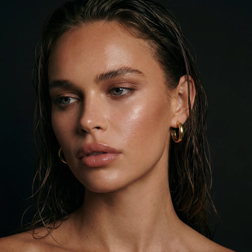 Smooth gold hoop earrings exuding elegance, perfectly complementing a natural makeup look in softly lit surroundings.