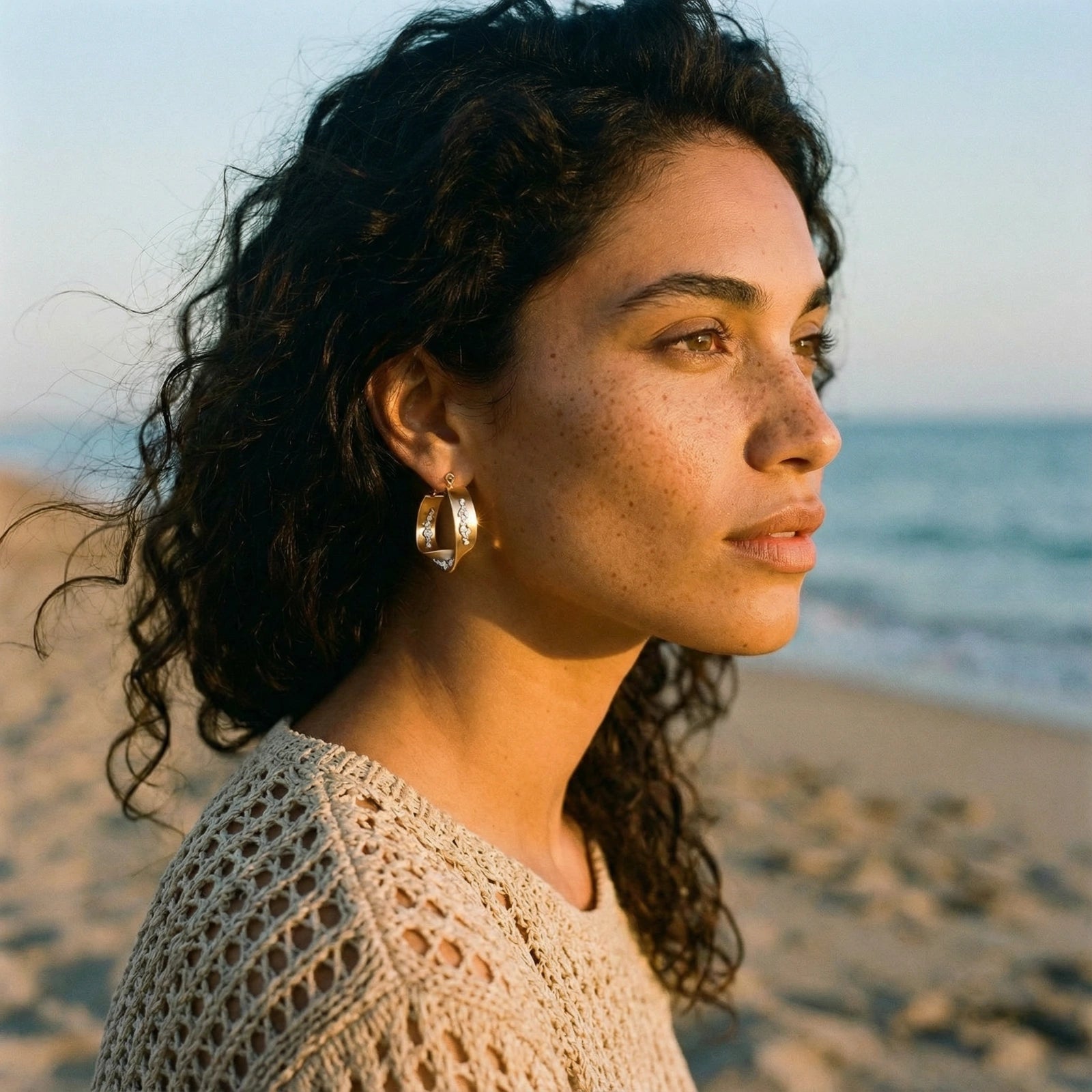 Sculptural twisted gold hoops reflecting light, adorned with shimmering silver crystals, worn in an outdoor setting.