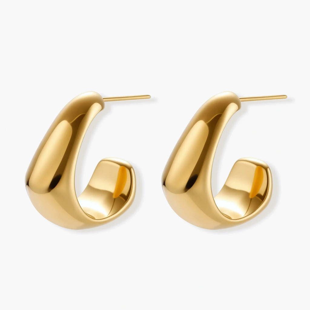 Close-up of curved gold-plated huggie earrings with sculptural design on white background, showing polished finish.