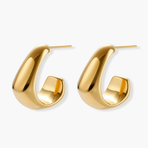 Close-up of curved gold-plated huggie earrings with sculptural design on white background, showing polished finish.