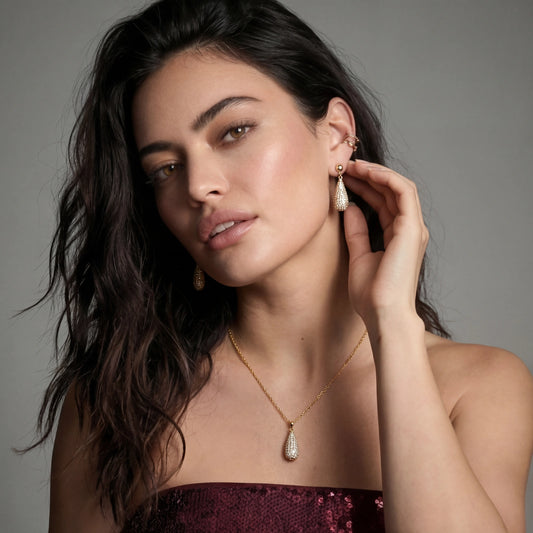 Gold-plated teardrop necklace and earrings covered in AAA cubic zirconia crystals on cream background.