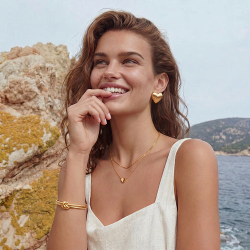 A woman elegantly showcases the Golden Knot Cuff, a gold bracelet with a sophisticated knot design, set against a serene outdoor backdrop.