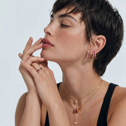Model showcasing the Royal Ruby Stack Set, featuring a necklace, huggie hoop earrings, and adjustable ring with raspberry-red stones.