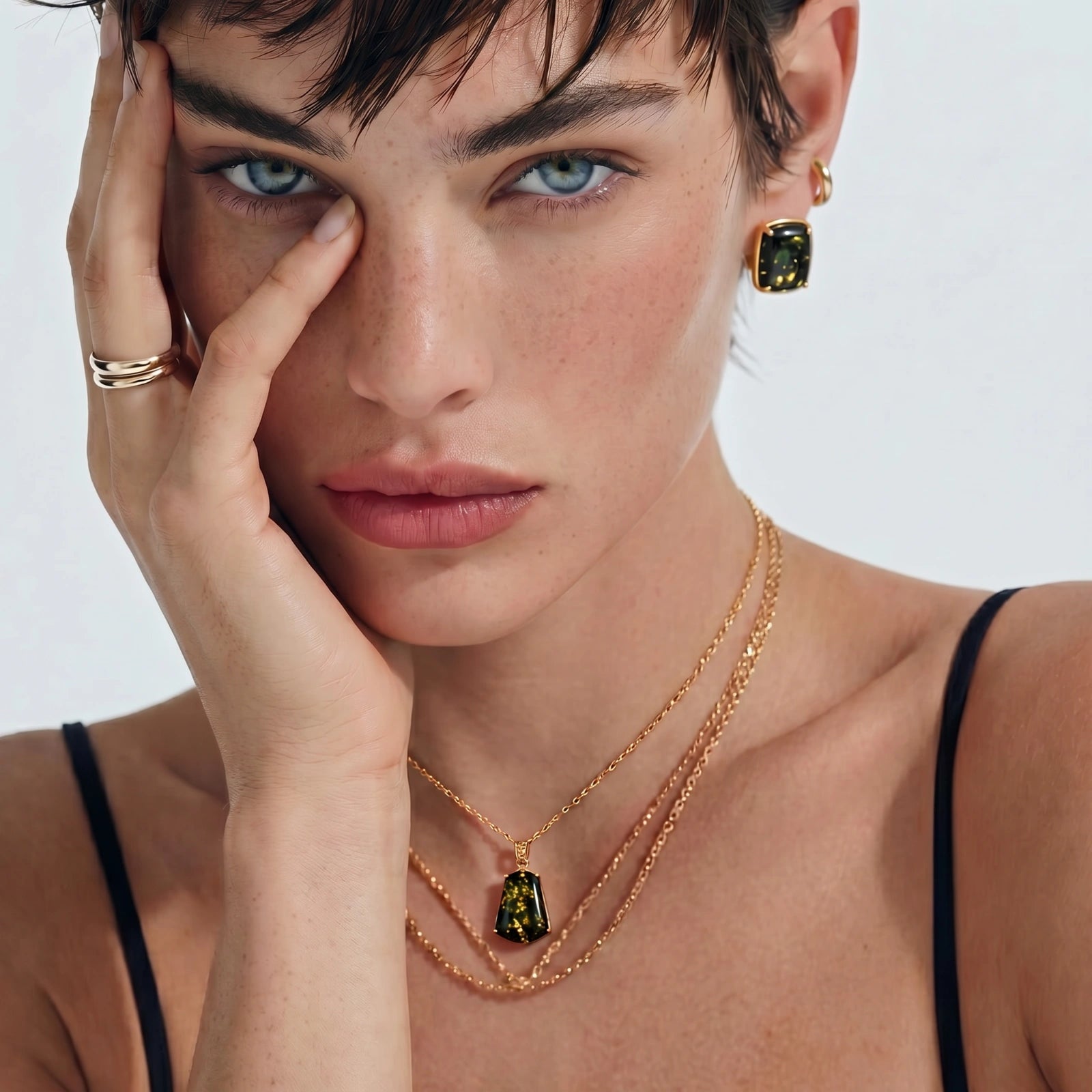Cushion-shaped earrings showcasing green amber with golden flecks, elegantly worn by a model with layered necklaces.