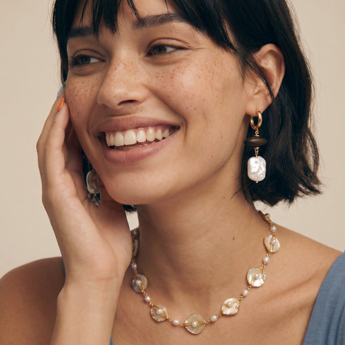 Necklace featuring shell fragments and round pearls, elegantly worn by a model in a soft, neutral setting.